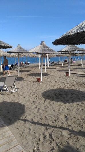 A beach with thatched umbrellas, lounge chairs, and a wooden walkway. - The Santo George Seaside Boutique (Malevizi)