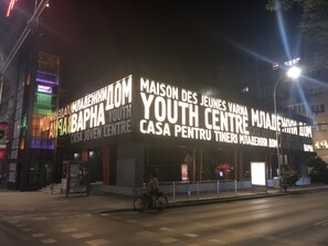 Ein Gebäude mit großen, beleuchteten Schildern, auf denen „Maison des Jeunes Varnase Youth Centre“ und „Casa para jóvenes“ stehen.