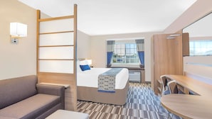 Una habitación de hotel con cama, sofá, mesa de comedor y ventana con cortinas.