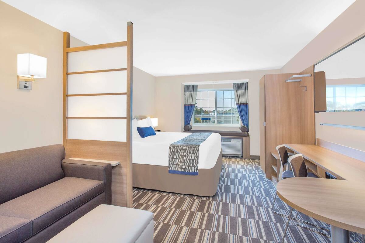 Una habitación de hotel con cama, sofá, mesa de comedor y ventana con cortinas.