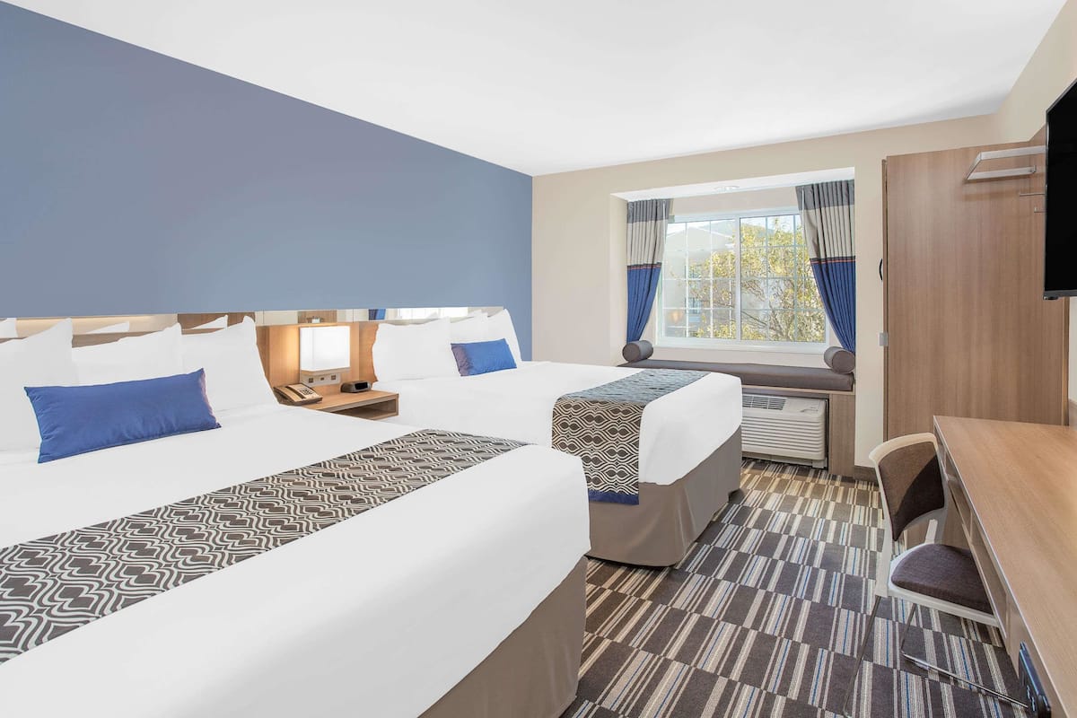 Habitación de hotel con una cama grande, un escritorio, una silla, un televisor y una ventana con cortinas.