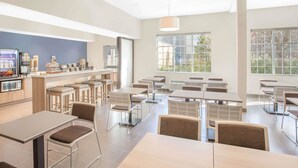 Un comedor moderno con mesas y sillas altas, una barra con productos alimenticios y amplios ventanales que aportan luz natural.