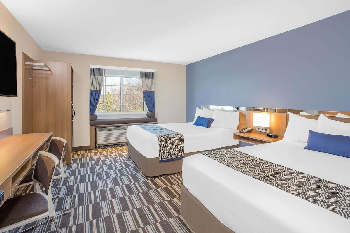 Habitación de hotel con dos camas, un escritorio, sillas, televisor y ventana con cortinas.