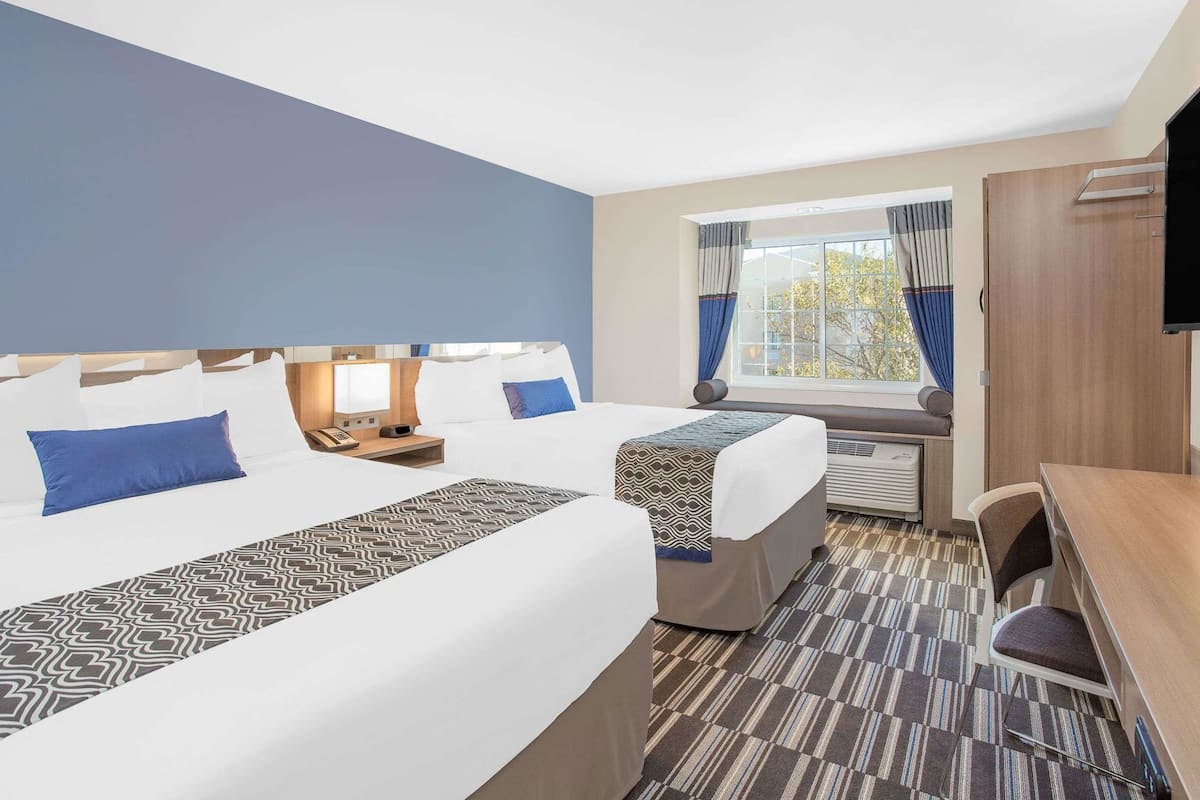 Habitación de hotel con dos camas, un escritorio, un televisor y una ventana con cortinas.