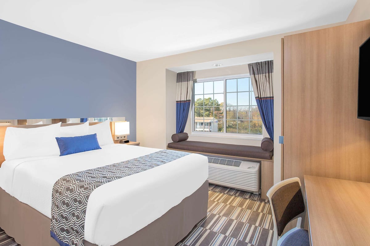 Habitación de hotel con una cama grande, un escritorio, una ventana con cortinas y un televisor de pantalla plana montado en la pared.