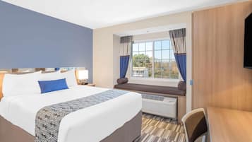 A hotel room with a large bed, a desk, a window with curtains, and a flat-screen TV mounted on the wall.
