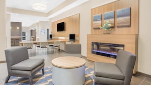 Un moderno vestíbulo de hotel con una mesa redonda, sillones grises, un televisor de pantalla plana y una chimenea.