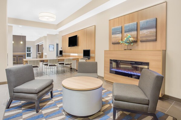 Un moderno vestíbulo de hotel con una mesa redonda, sillones grises, un televisor de pantalla plana y una chimenea.