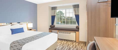 Habitación de hotel con una cama grande, una banca junto a la ventana, un escritorio y un televisor fijado a la pared.