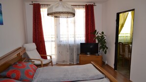 A hotel room with a bed, a chair, a TV, a plant, and a balcony with red curtains. - Apartment Alejní (Teplice)