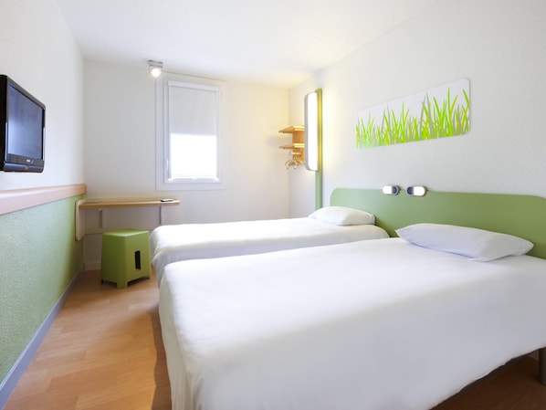 Quarto de hotel com duas camas, uma escrivaninha, um banquinho, uma televisão, uma janela e uma obra de arte na parede.