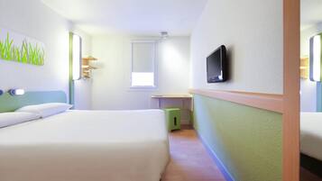 Habitación de hotel con dos camas, televisión, una ventana pequeña y un cesto de basura verde.