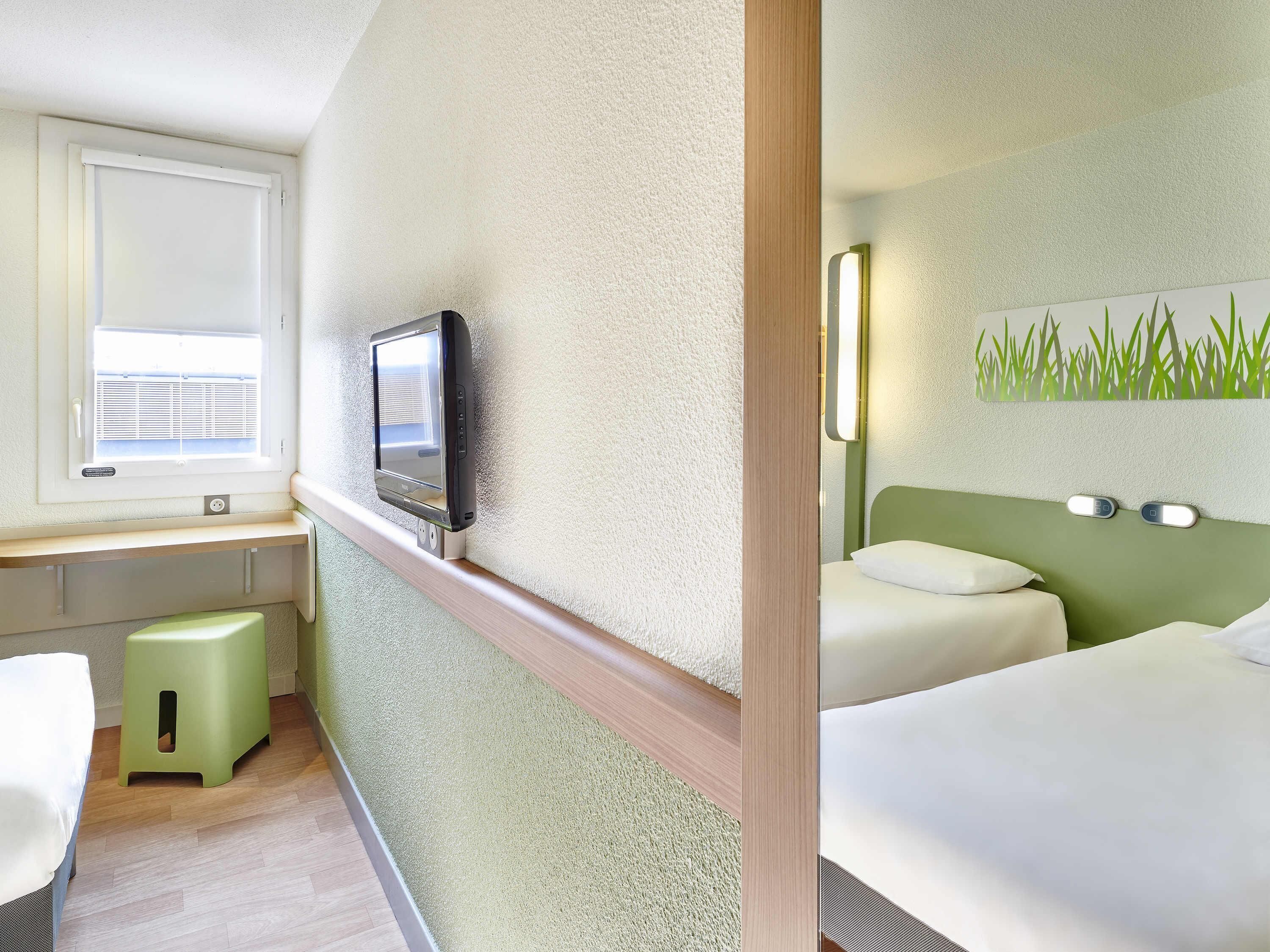 Een hotelkamer met een bed, een bureau met een televisie, een klein krukje en een wandlamp.
