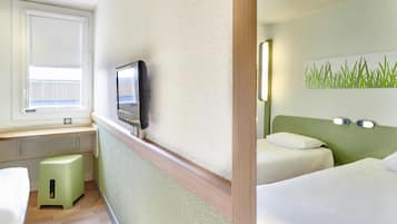 Ein Hotelzimmer mit einem Bett, einem Schreibtisch mit Fernseher, einem kleinen Hocker und einer Wandleuchte.
