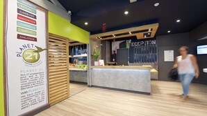 A reception area with a wooden counter, a green wall, and a sign about the Planet 21 initiative. - ibis Budget Dax Saint Paul les Dax (Saint-Paul-les-Dax)