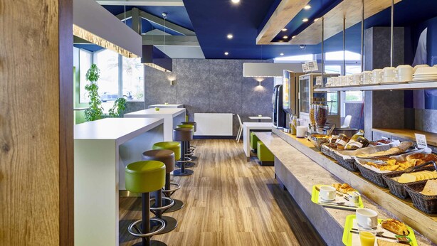 A modern breakfast bar with stools, a coffee machine, and a variety of breakfast items. - ibis Budget Dax Saint Paul les Dax (Saint-Paul-les-Dax)