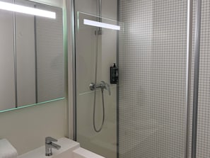 Un baño moderno con ducha de vidrio, lavamanos blanco y espejo con iluminación.