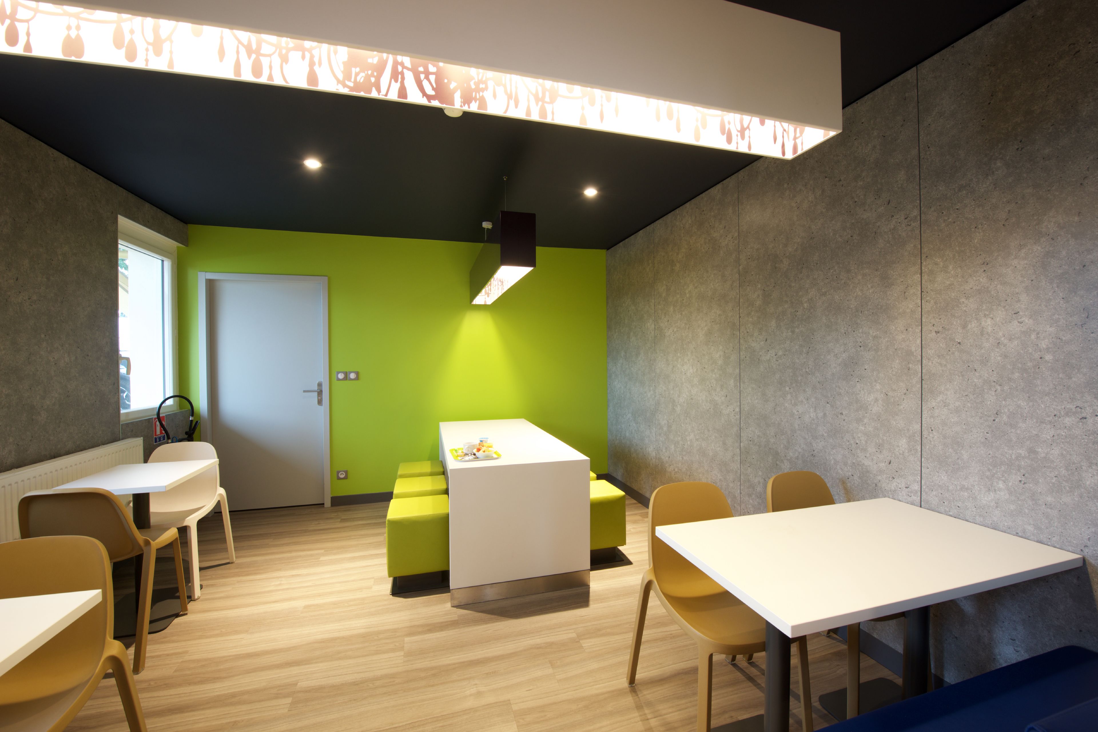 A modern meeting room with a white table, yellow chairs, and a green accent wall.