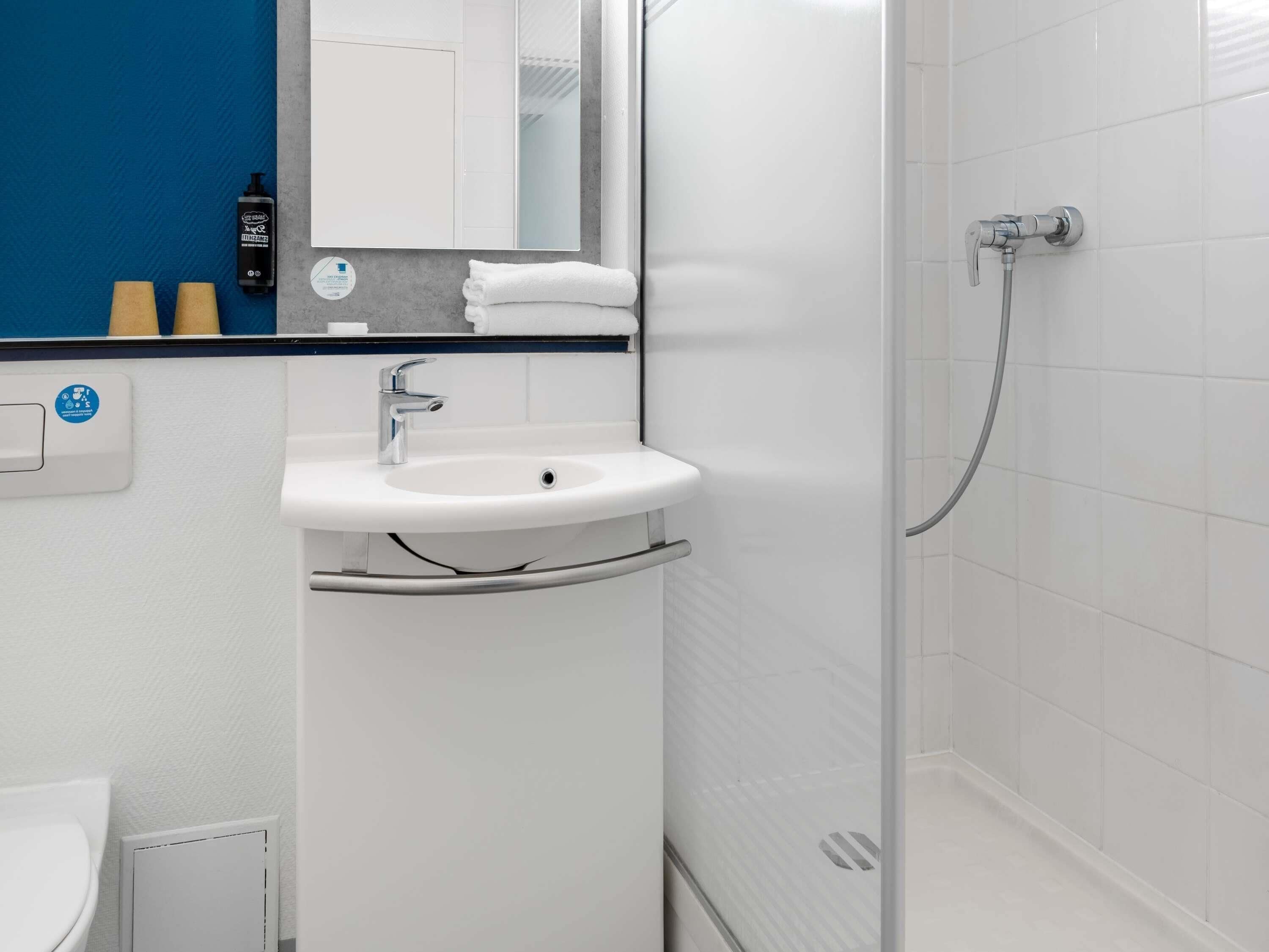 A bathroom with a white sink, a mirror, a shower, and a blue accent wall.