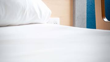Una cama bien tendida con una almohada blanca y un enchufe en la pared.