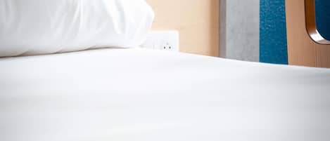Una cama bien tendida con una almohada blanca y un enchufe en la pared.