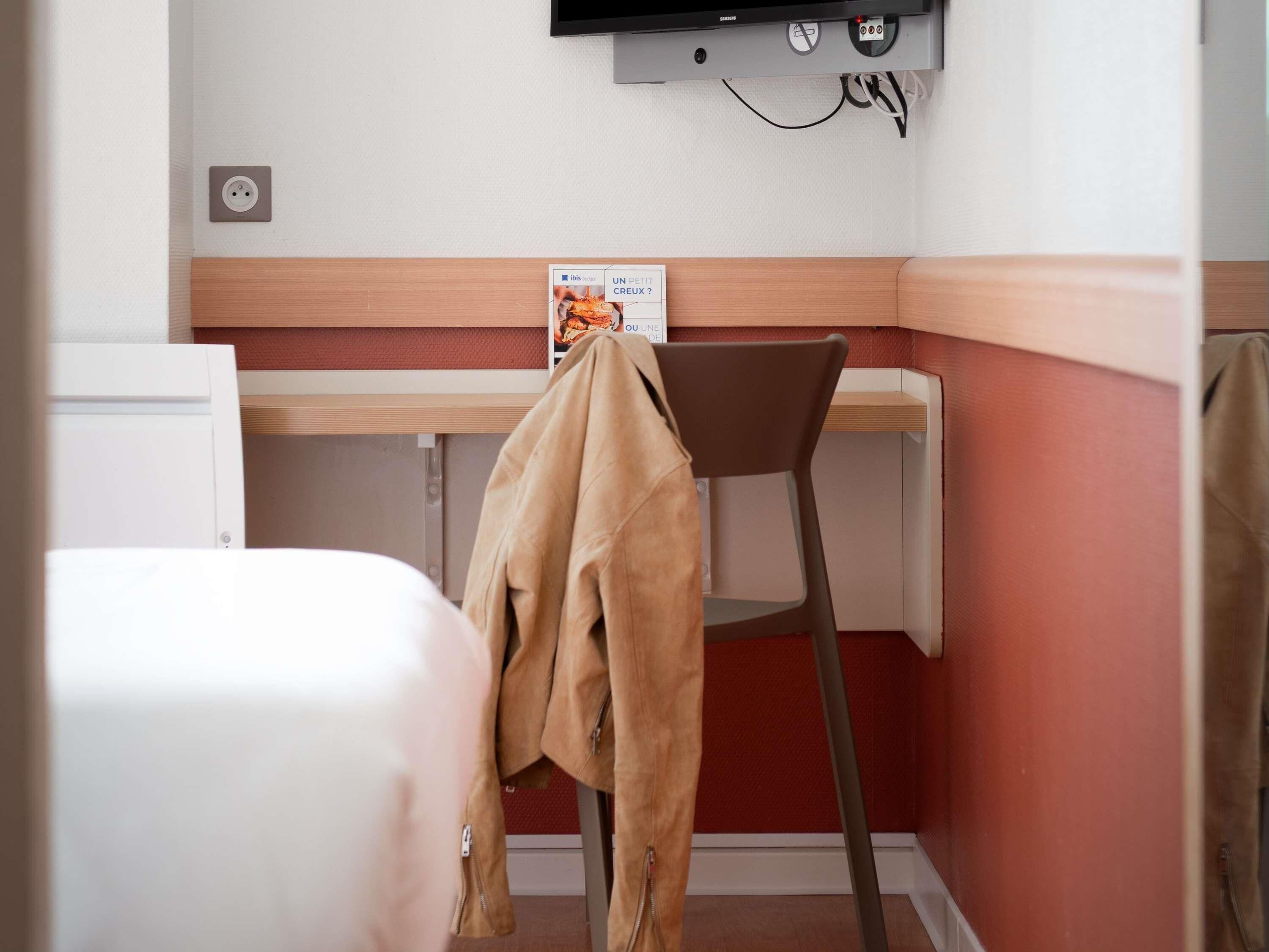 Habitación de hotel con una cama, un escritorio, una silla y un televisor montado en la pared.