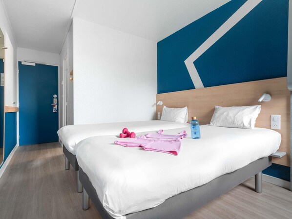 A hotel room with a large bed, white bedding, a blue wall with a geometric design, and a wooden headboard. - ibis Budget Caen Mondeville (Mondeville)