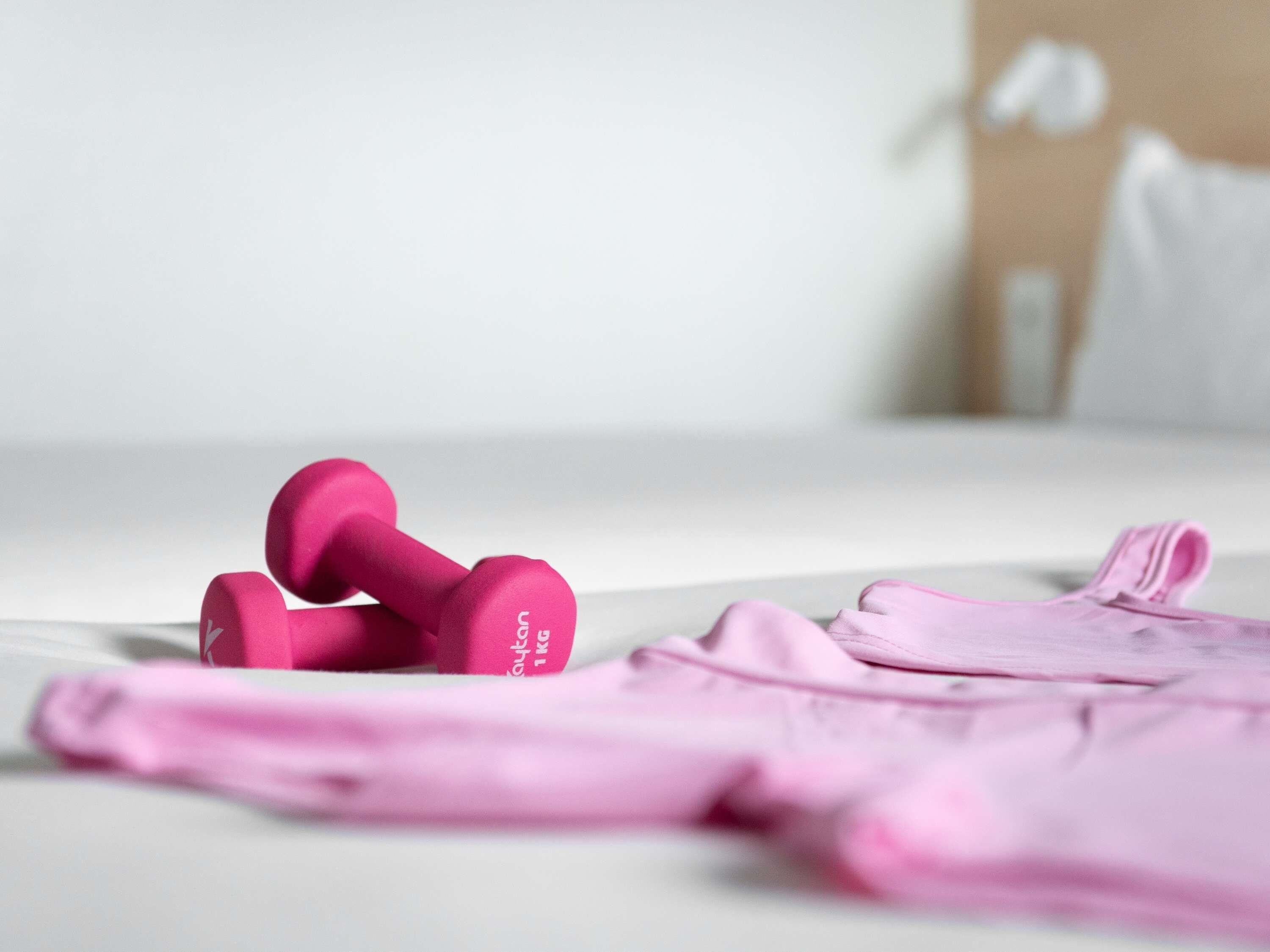 A bed with pink bedding and a pair of pink dumbbells on it.