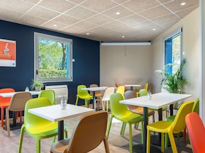 A modern dining area with colorful chairs and tables, large windows with natural light, and a ceiling with recessed lighting. - ibis Budget Caen Mondeville (Mondeville)