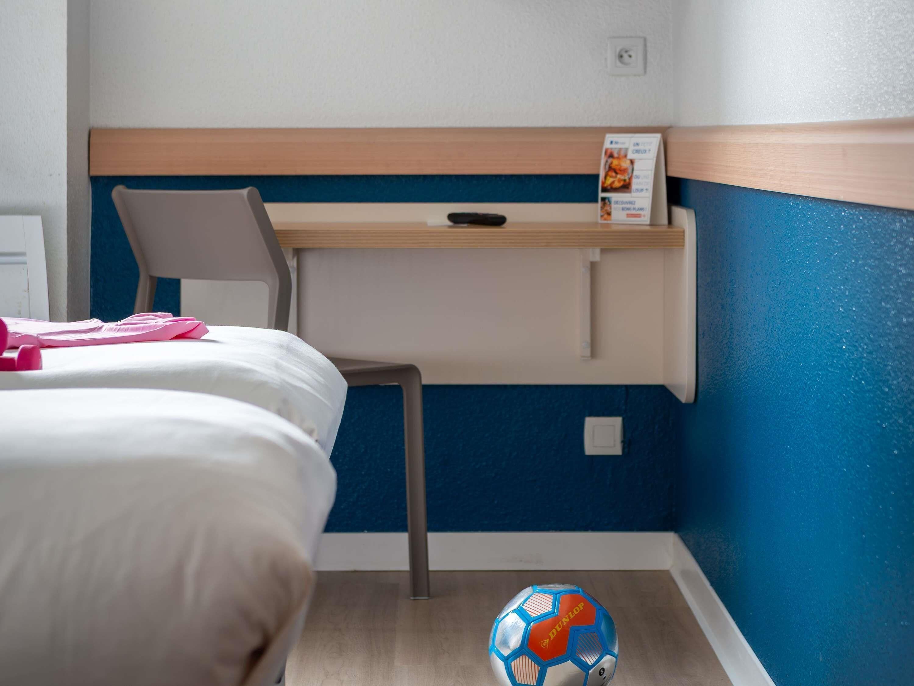 Ein Schlafzimmer mit einem Bett, einem Sessel, einem Schreibtisch und einem an der Wand befestigten Regal.