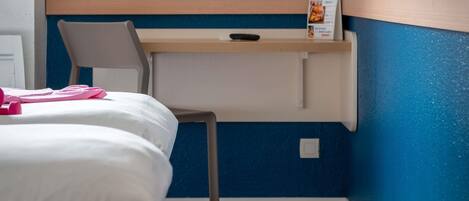A bedroom with a bed, a chair, a desk, and a wall-mounted shelf.