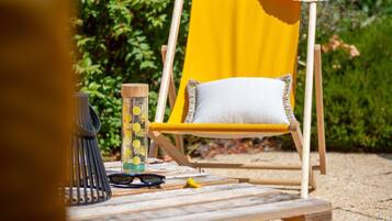A wooden deck with a yellow chair, a clear bottle with yellow objects, a pair of sunglasses, and a small wooden block.
