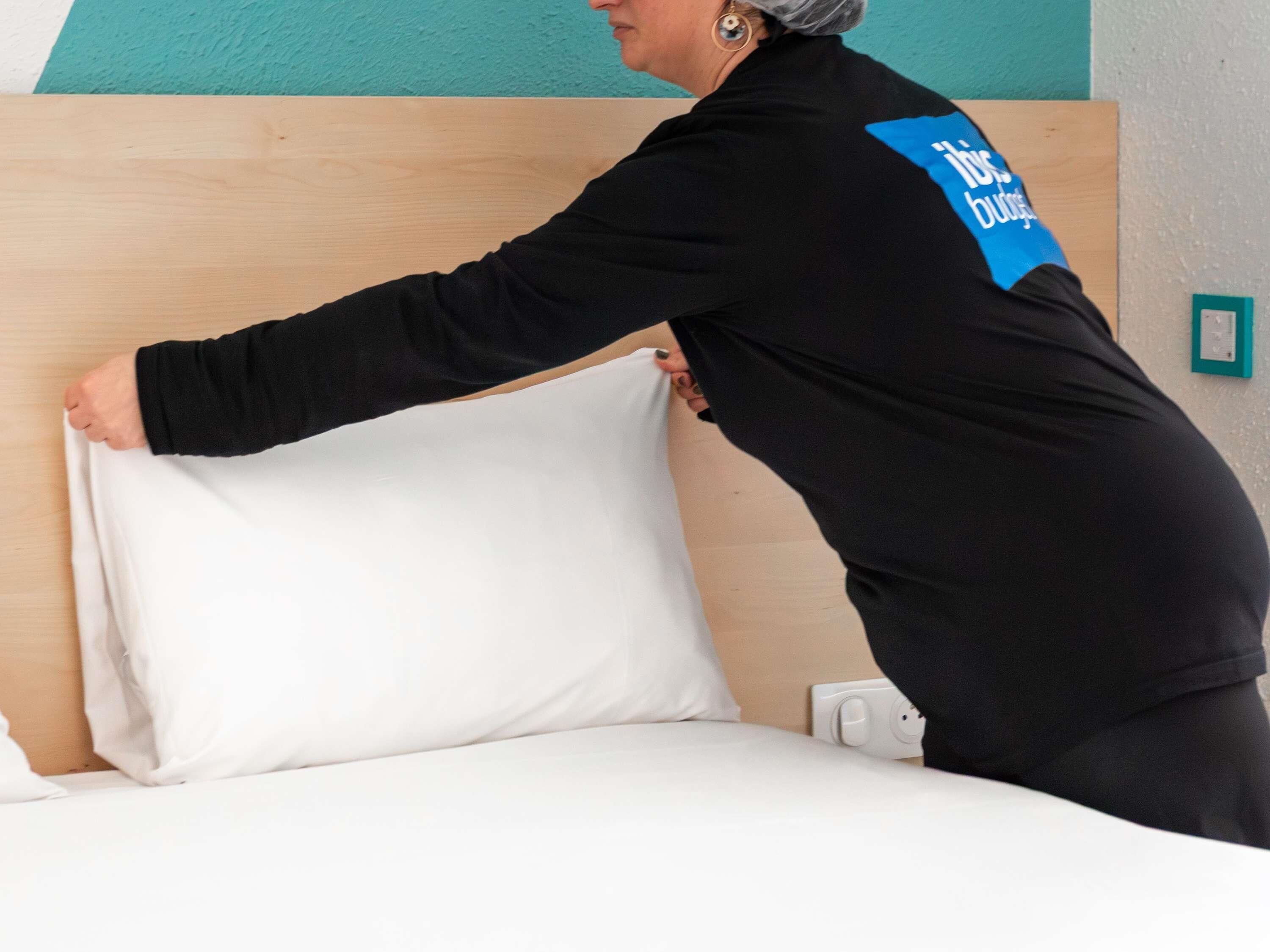 Iemand die een wit kussen op een bed opmaakt in een kamer met teal muren en een houten hoofdbord.