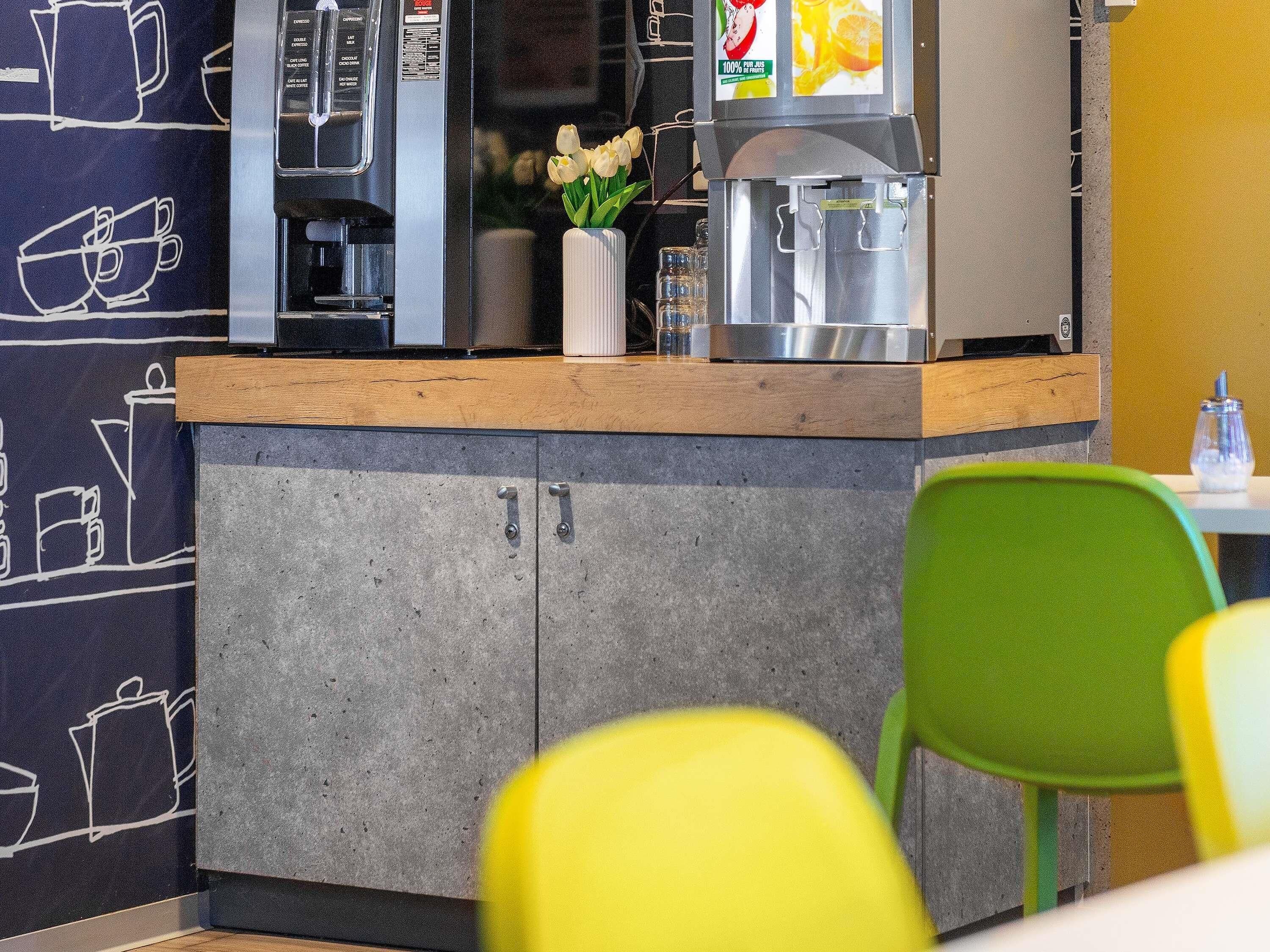Una máquina de café, un dispensador de agua y un florero con flores sobre una encimera.