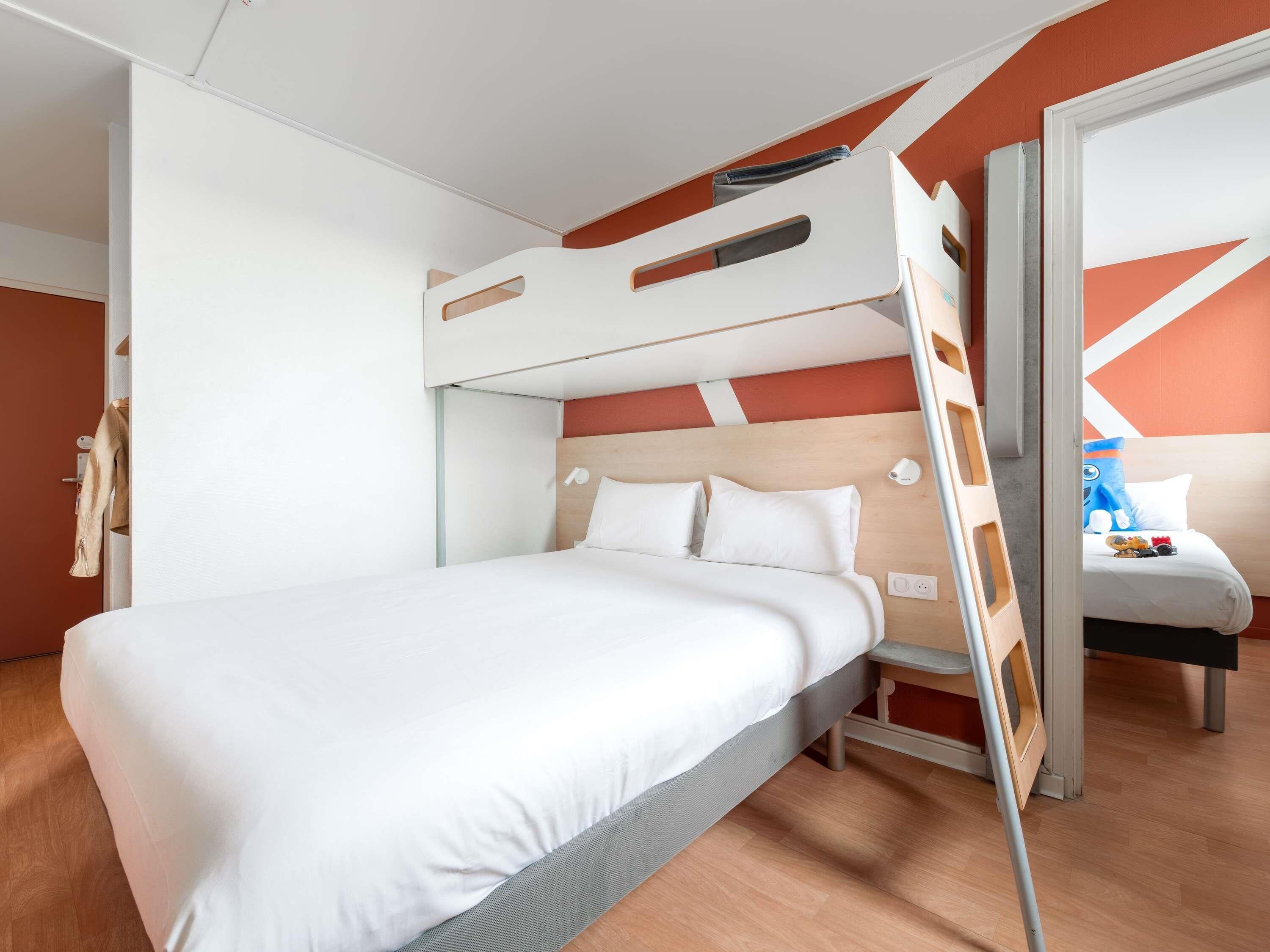 A bunk bed with a wooden headboard, a bedside table, and a small seating area with a cushion and a toy.