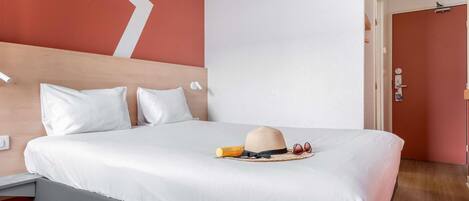 Una cama bien hecha con sábanas blancas, cabecera de madera y una pared de acento roja.