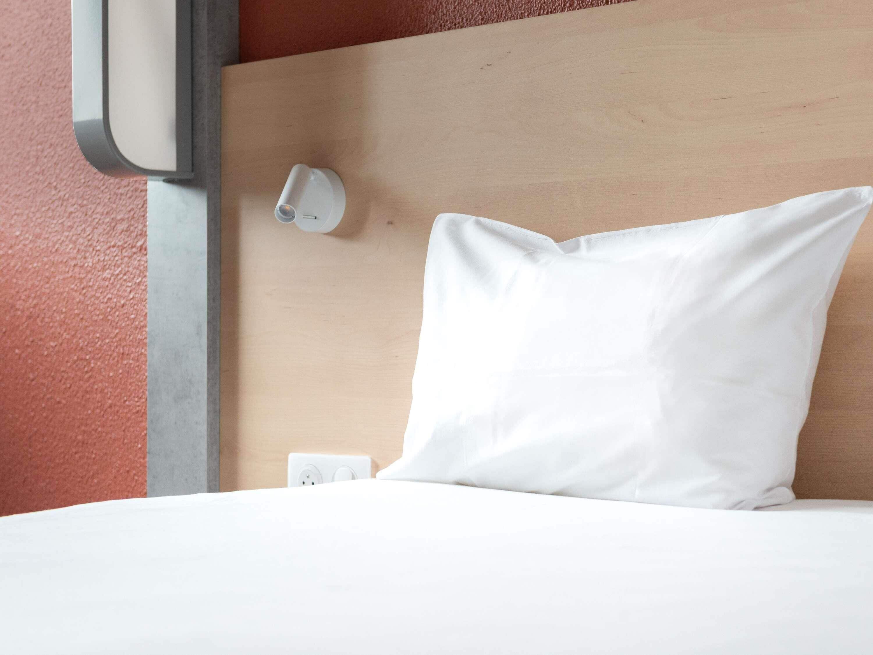 A neatly made bed with a white pillow and a headboard with a light switch.