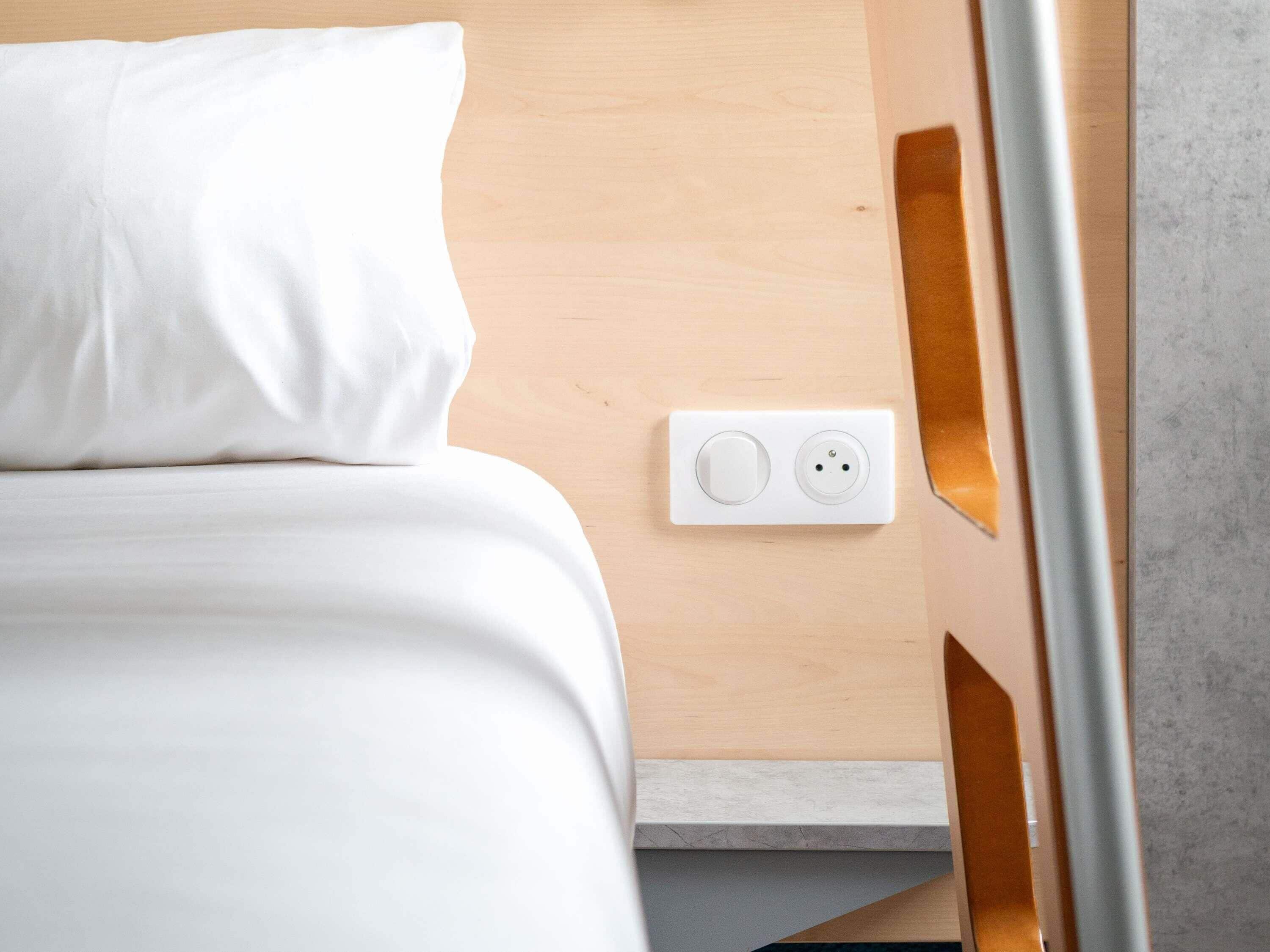 Een bed met wit beddengoed, een houten hoofdbord en een wandcontactdoos.