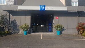 La entrada al hotel ibis budget, con un cartel sobre las puertas, un letrero de prohibido fumar y dos plantas en macetas a cada lado.