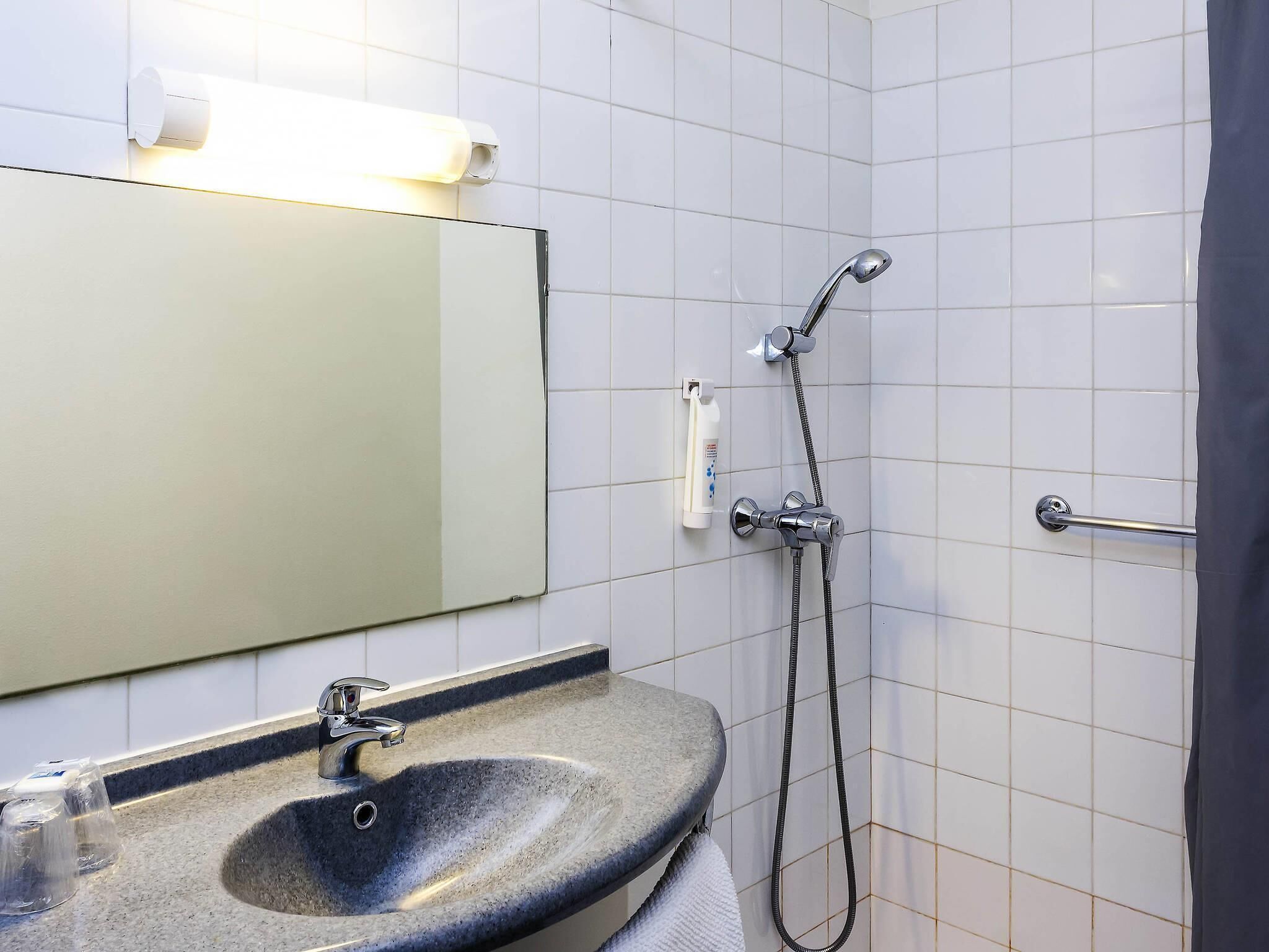 Un baño con lavabo, espejo, ducha y toallero.