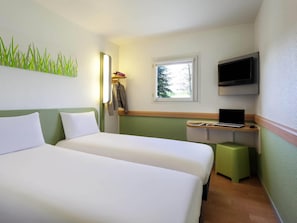 Een hotelkamer met twee bedden, een bureau met een laptop, een televisie en een raam met uitzicht op bomen.