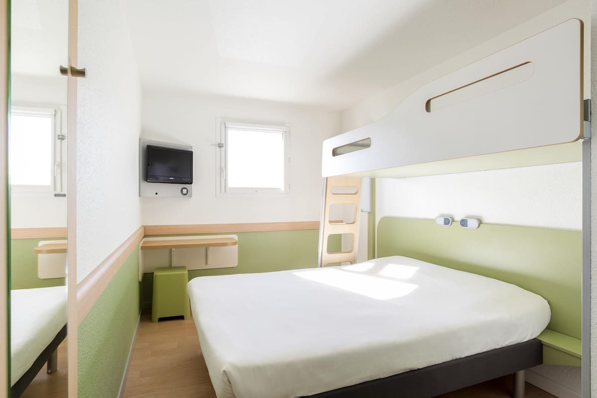 Een enkel bed met hoofdeinde, een nachtkastje, een aan de muur bevestigde televisie en een raam.