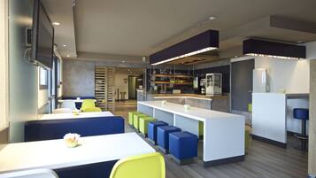 A modern restaurant with high tables, colorful seating, and a bar area.