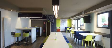 A modern dining area with a long table, colorful chairs, and a flat-screen TV mounted on the wall.