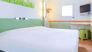 Une chambre d’hôtel avec un lit, un téléviseur fixé au mur, une fenêtre et un petit tabouret.