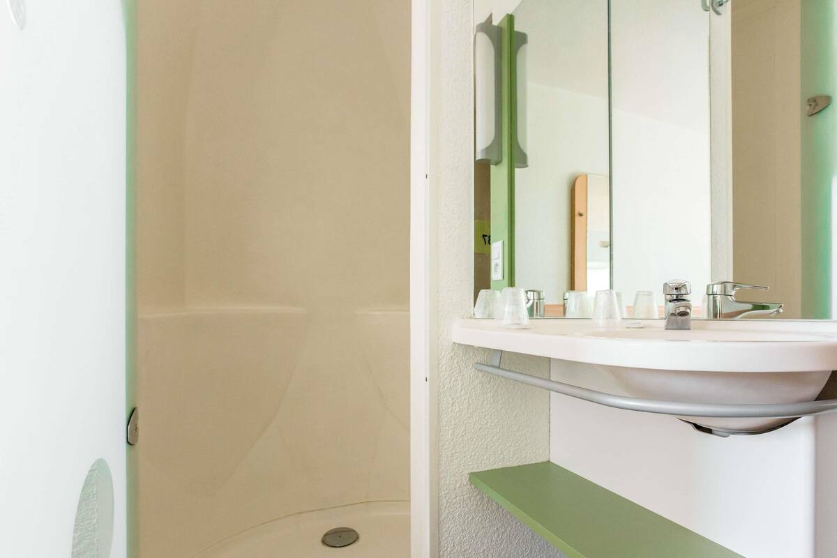 Een badkamer met een witte wastafel, een spiegel en een douchegedeelte.