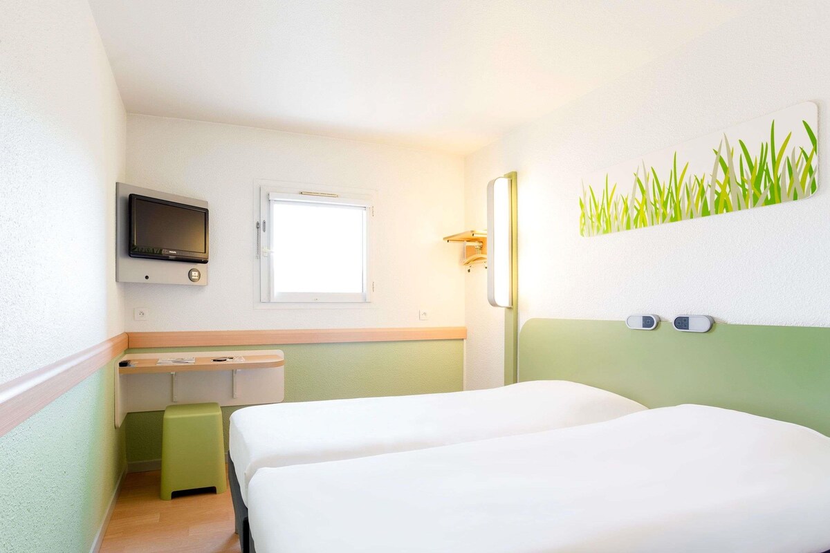 Une chambre d’hôtel avec deux lits, un bureau, une télévision et une fenêtre.