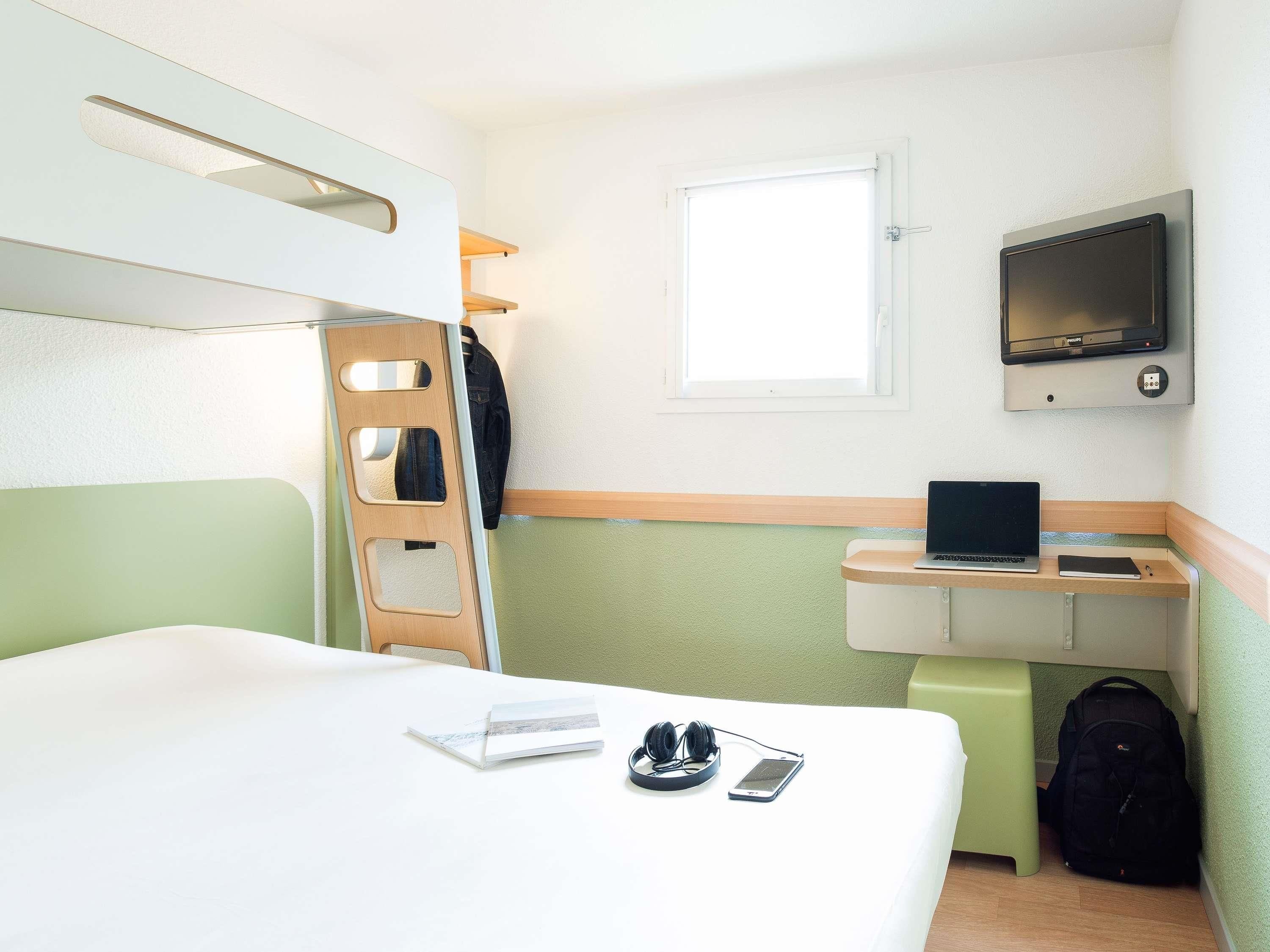 Una habitación de hotel con una cama, un escritorio con una computadora portátil, un televisor y una ventana.