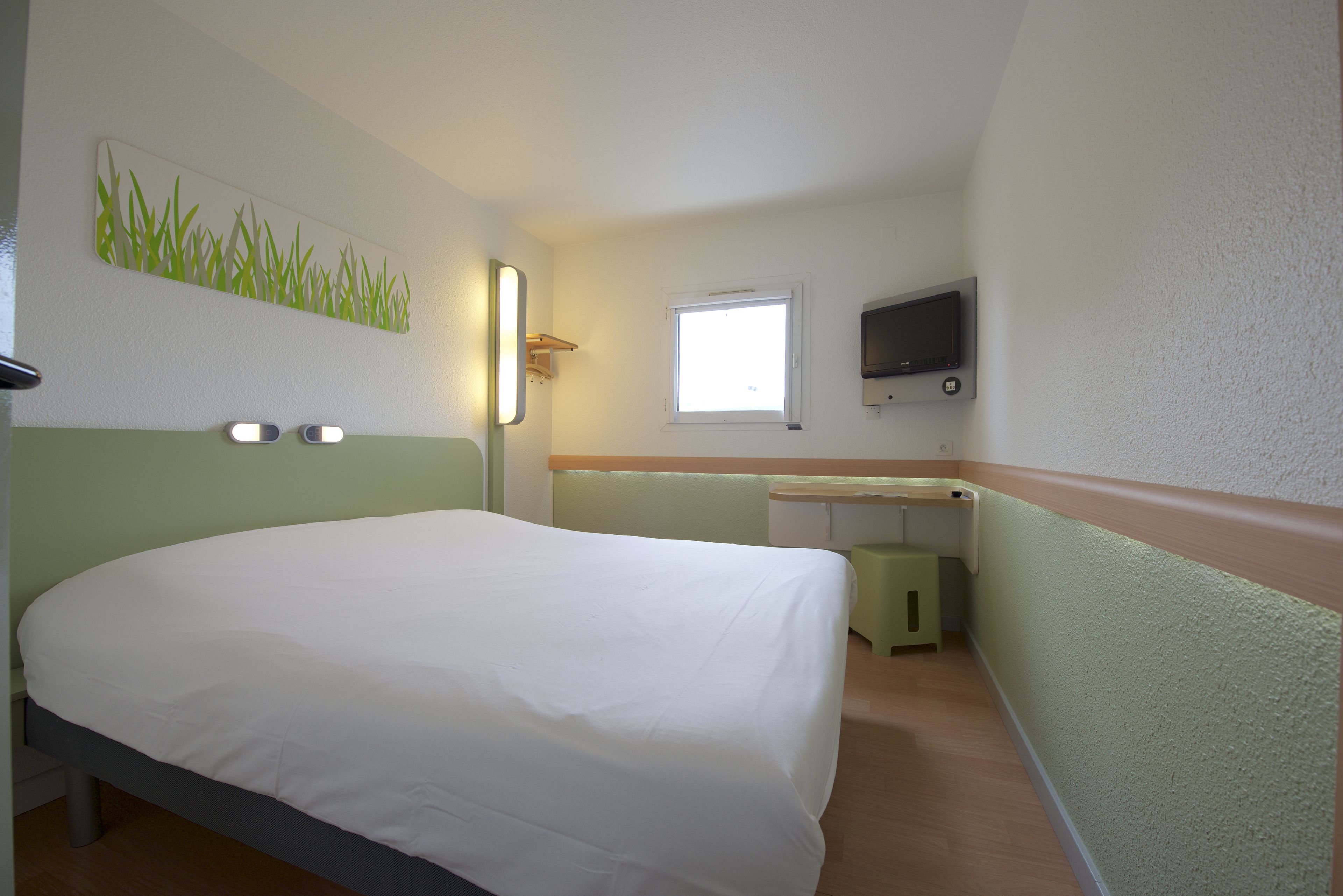 Una habitación de hotel con una cama, un escritorio, un televisor y una ventana.