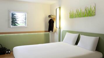 Quarto de hotel com cama, janela, cabideiro e luminária na parede.